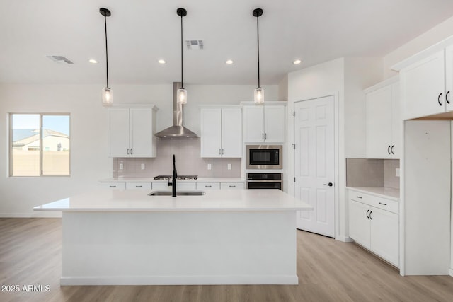 kitchen with oven, a kitchen island with sink, built in microwave, and wall chimney exhaust hood