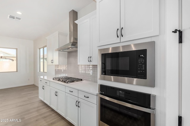 kitchen featuring appliances with stainless steel finishes, wall chimney range hood, decorative backsplash, and white cabinetry