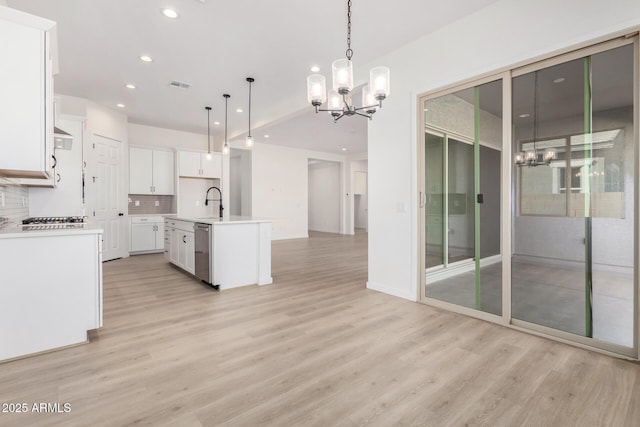 kitchen featuring decorative light fixtures, white cabinets, tasteful backsplash, a chandelier, and a kitchen island with sink