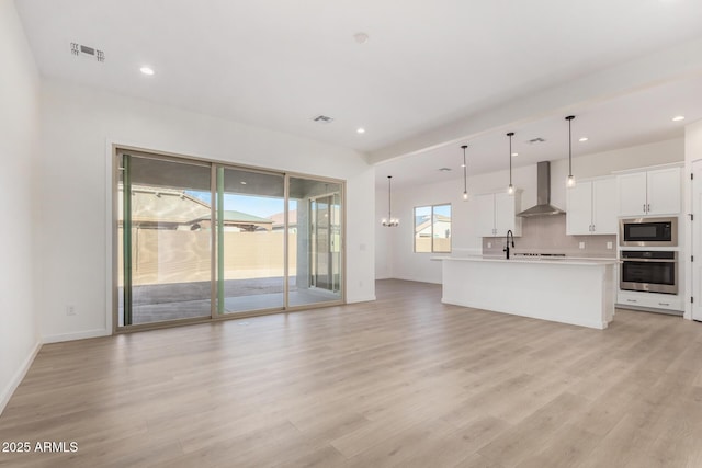 kitchen featuring stainless steel oven, hanging light fixtures, wall chimney range hood, built in microwave, and white cabinets