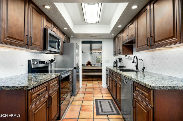 kitchen with sink, a raised ceiling, stone countertops, decorative backsplash, and appliances with stainless steel finishes