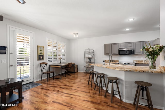 kitchen featuring a breakfast bar, gray cabinets, light stone counters, wood-type flooring, and stainless steel appliances