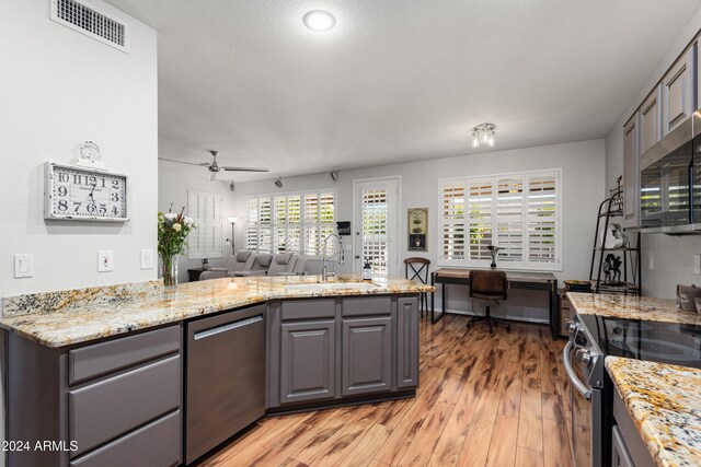 kitchen featuring sink, ceiling fan, light wood-type flooring, appliances with stainless steel finishes, and light stone counters