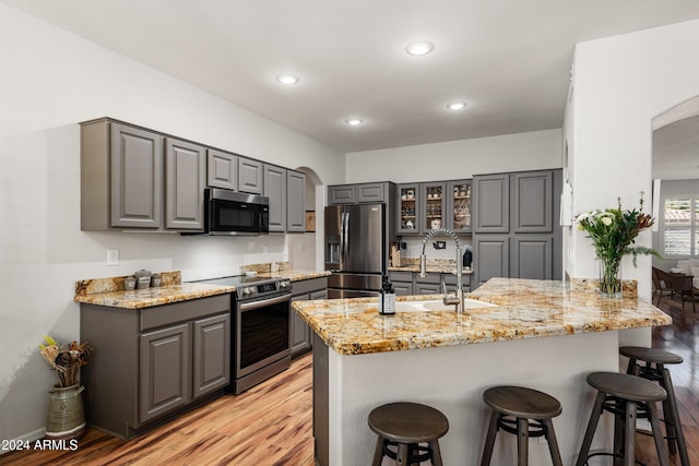 kitchen with gray cabinetry, light stone countertops, light hardwood / wood-style floors, kitchen peninsula, and stainless steel appliances