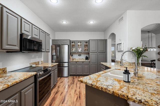 kitchen featuring gray cabinetry, sink, light stone counters, light hardwood / wood-style floors, and appliances with stainless steel finishes