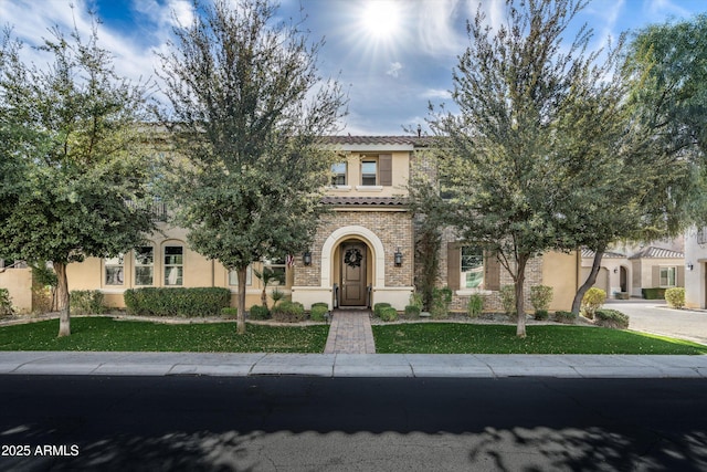 view of front of property featuring a tiled roof, brick siding, a front lawn, and stucco siding