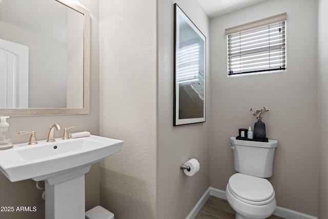 half bathroom featuring toilet, baseboards, a sink, and wood finished floors