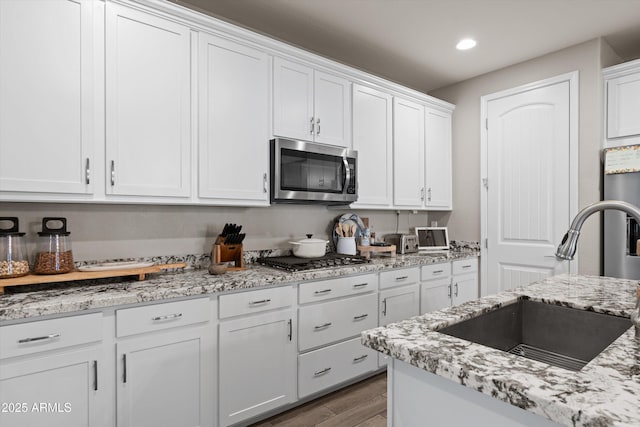 kitchen featuring light stone counters, wood finished floors, a sink, white cabinetry, and appliances with stainless steel finishes