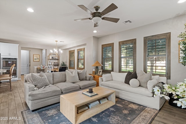 living area featuring ceiling fan with notable chandelier, light wood finished floors, visible vents, and a healthy amount of sunlight