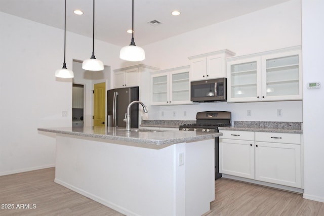 kitchen featuring light wood-style flooring, appliances with stainless steel finishes, white cabinets, a sink, and an island with sink