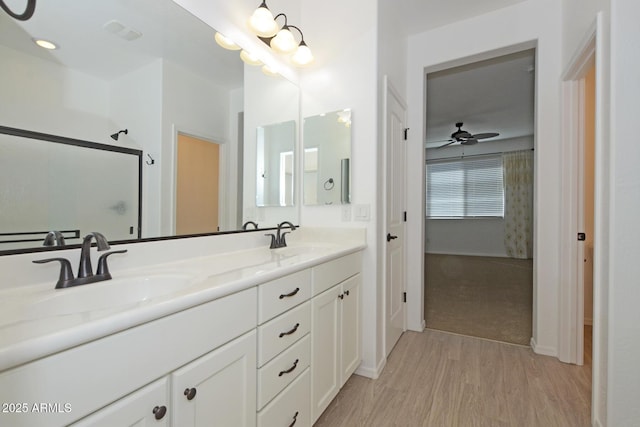 bathroom featuring double vanity, wood finished floors, a sink, and a shower with shower door