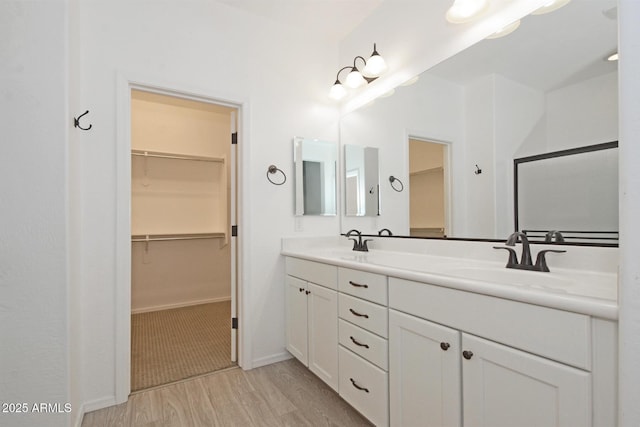 bathroom with wood finished floors, a sink, a spacious closet, and double vanity