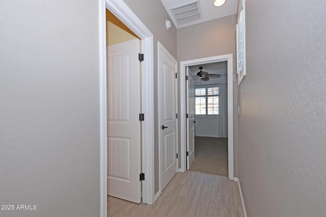 hall featuring light wood-style floors, visible vents, a textured wall, and baseboards