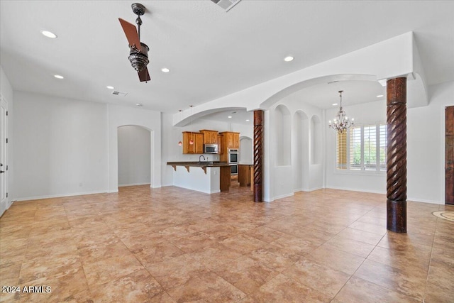 unfurnished living room featuring ceiling fan with notable chandelier, light tile flooring, and decorative columns