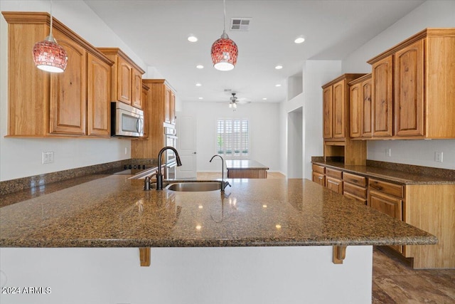 kitchen with hanging light fixtures, ceiling fan, sink, and dark stone counters