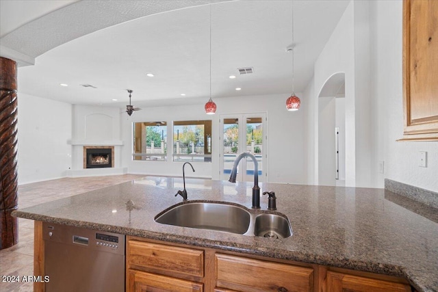 kitchen featuring dark stone counters, ceiling fan, dishwasher, decorative light fixtures, and sink