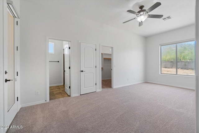 unfurnished bedroom with a walk in closet, carpet floors, a closet, ensuite bathroom, and ceiling fan