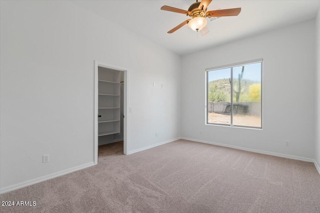 unfurnished bedroom with a walk in closet, a closet, carpet floors, and ceiling fan