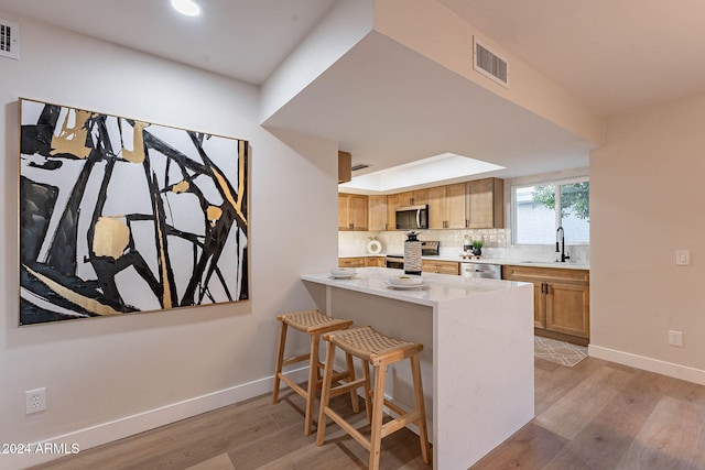 kitchen featuring kitchen peninsula, appliances with stainless steel finishes, a breakfast bar, sink, and light hardwood / wood-style floors