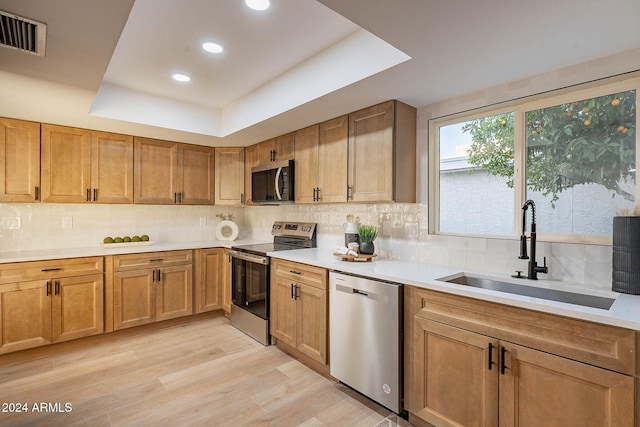 kitchen featuring a raised ceiling, sink, decorative backsplash, light wood-type flooring, and stainless steel appliances