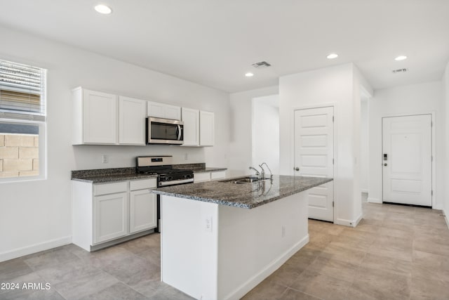 kitchen with sink, appliances with stainless steel finishes, dark stone countertops, white cabinets, and a center island with sink