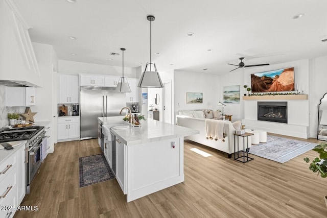 kitchen with decorative light fixtures, premium range hood, a kitchen island with sink, premium appliances, and white cabinets