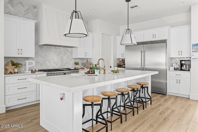 kitchen with white cabinets, pendant lighting, stainless steel built in fridge, and a center island with sink