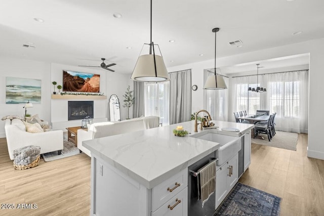 kitchen with light stone countertops, sink, an island with sink, and decorative light fixtures