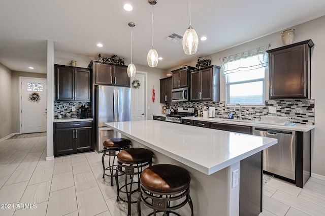 kitchen with a breakfast bar, stainless steel appliances, sink, a kitchen island, and hanging light fixtures