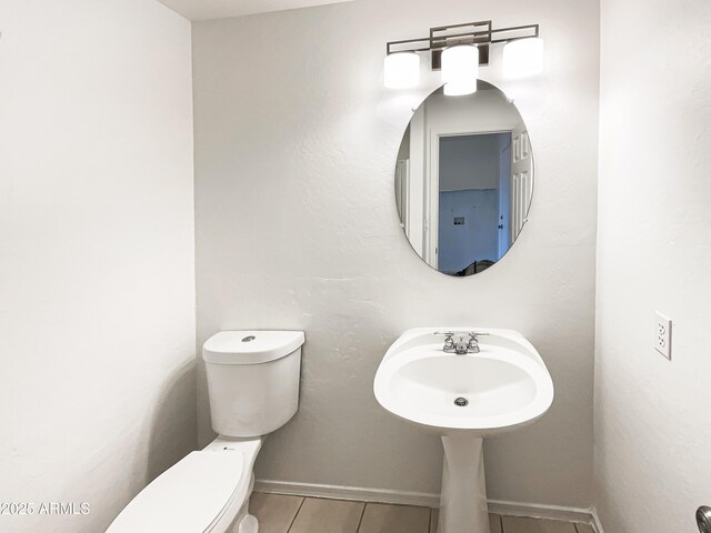 half bathroom with toilet, baseboards, a sink, and tile patterned floors