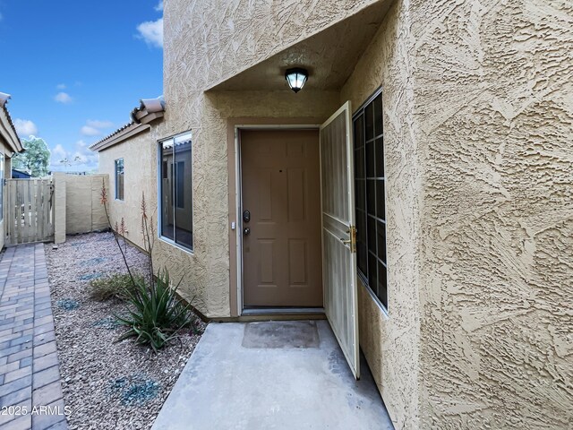 entrance to property featuring fence and stucco siding