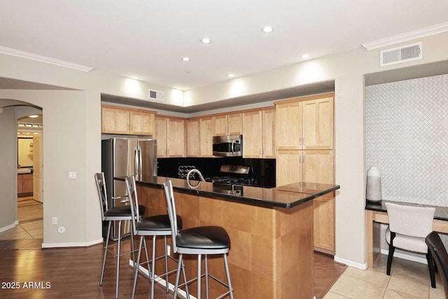 7601 E Indian Bend Rd Unit 1040, Scottsdale, AZ 85250 - kitchen with appliances with stainless steel finishes, arched walkways, light brown cabinetry, a breakfast bar area, and dark countertops