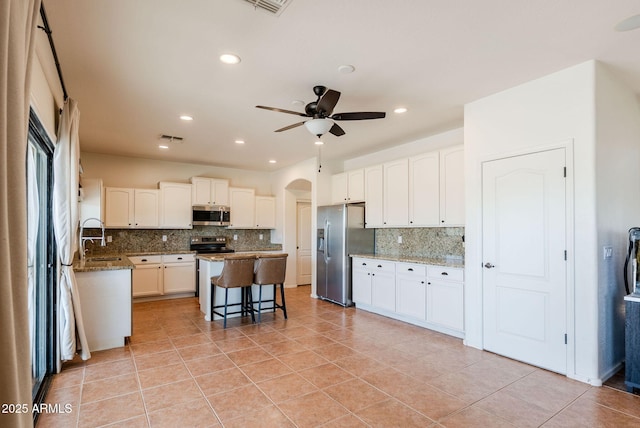 9998 W Prospector Dr, Queen Creek, AZ 85144 - kitchen featuring appliances with stainless steel finishes, decorative backsplash, a center island, a kitchen breakfast bar, and light stone countertops