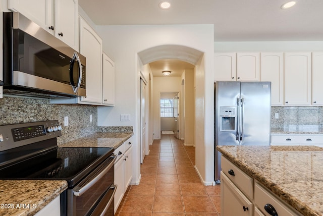 9998 W Prospector Dr, Queen Creek, AZ 85144 - kitchen featuring appliances with stainless steel finishes, arched walkways, light tile patterned floors, light stone counters, and recessed lighting