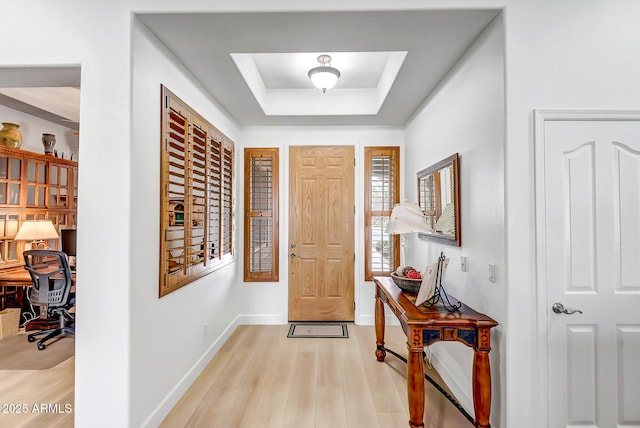 entryway featuring baseboards, a raised ceiling, and light wood-style floors