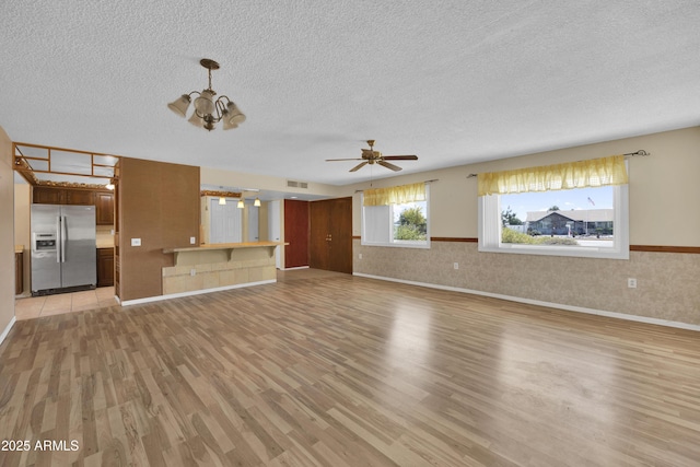 unfurnished living room featuring ceiling fan with notable chandelier, light hardwood / wood-style floors, and a textured ceiling