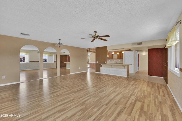 unfurnished living room featuring light wood-type flooring, a textured ceiling, and ceiling fan with notable chandelier