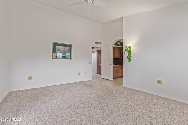 unfurnished room featuring visible vents, a ceiling fan, light tile patterned floors, light colored carpet, and a towering ceiling