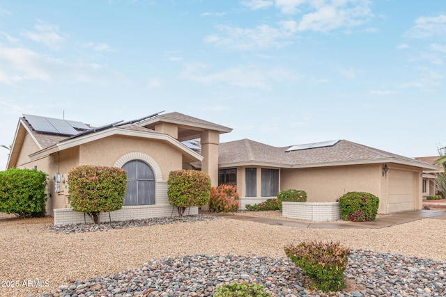 view of front facade featuring roof with shingles, a garage, roof mounted solar panels, and stucco siding