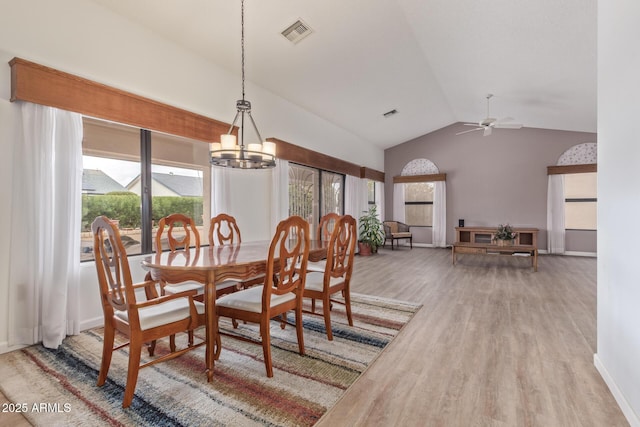 dining area with visible vents, baseboards, vaulted ceiling, ceiling fan with notable chandelier, and wood finished floors