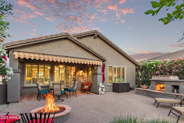343 W Twin Peaks Pkwy, San Tan Valley, AZ 85143 - back of house at dusk featuring a lit fireplace, stucco siding, a patio, and outdoor dining area