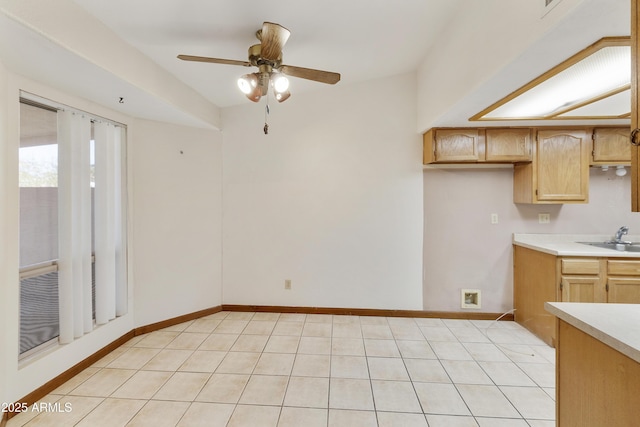 kitchen with a sink, light countertops, light tile patterned floors, baseboards, and ceiling fan