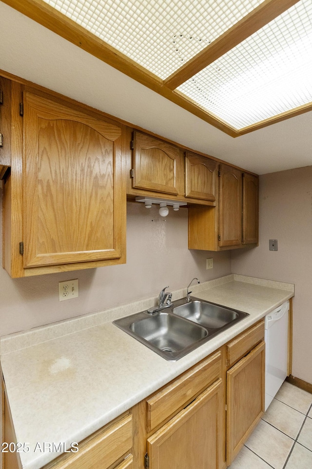 kitchen with light tile patterned floors, brown cabinetry, a sink, light countertops, and dishwasher