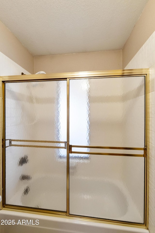 bathroom featuring bath / shower combo with glass door and a textured ceiling
