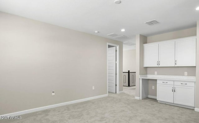 interior space featuring light carpet, built in desk, and white cabinets