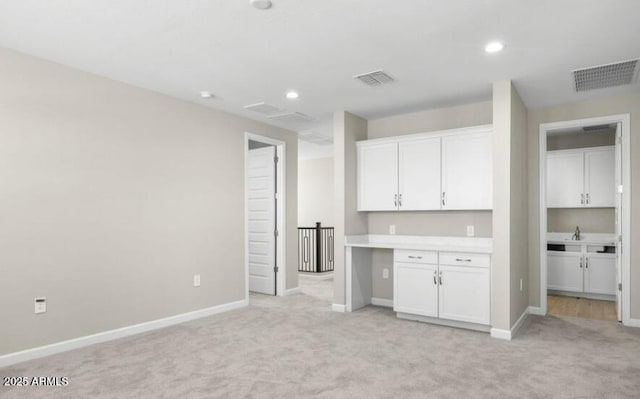 kitchen with white cabinetry, sink, built in desk, and light carpet