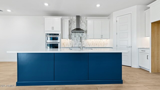 2316 W Moody Trl, Phoenix, AZ 85041 - kitchen featuring wall chimney exhaust hood, stainless steel double oven, a center island with sink, white cabinetry, and recessed lighting