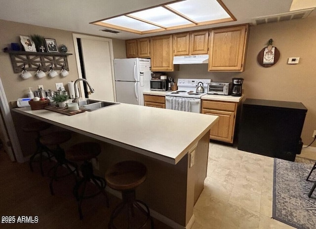 kitchen featuring white appliances, a skylight, a breakfast bar, under cabinet range hood, and a sink