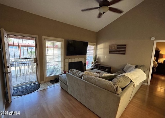 living area with light wood-style floors, a tile fireplace, vaulted ceiling, and ceiling fan