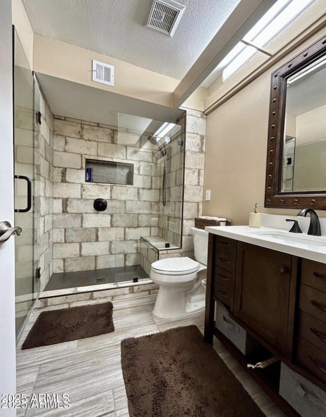 bathroom with visible vents, toilet, a shower stall, vanity, and a textured ceiling